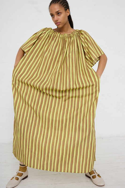 A woman posing in a Summer Dress in Brown and Yellow Stripes from the AVN womenswear collection, featuring oversized short sleeves and a gathered neckline, paired with casual shoes.