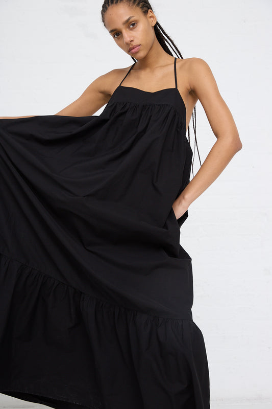 A woman holding out a flowing black AVN Sun Sational Dress against a white background.
