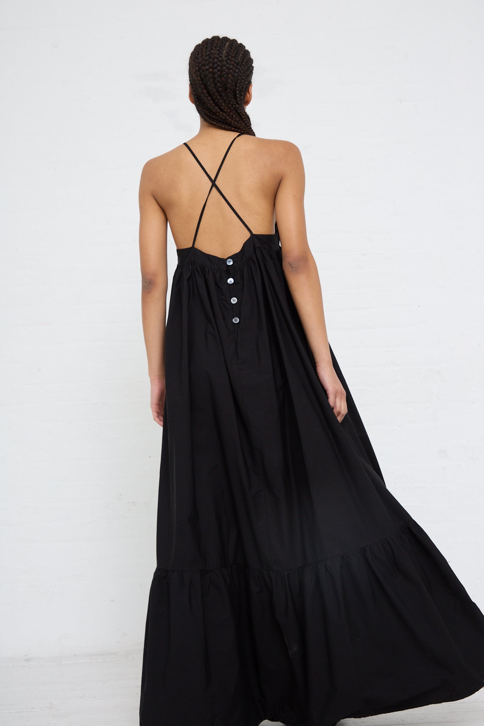 A woman seen from behind wearing a AVN Sun Sational Dress in Black with button detailing and a cross-back strap design, crafted from lightweight cotton.