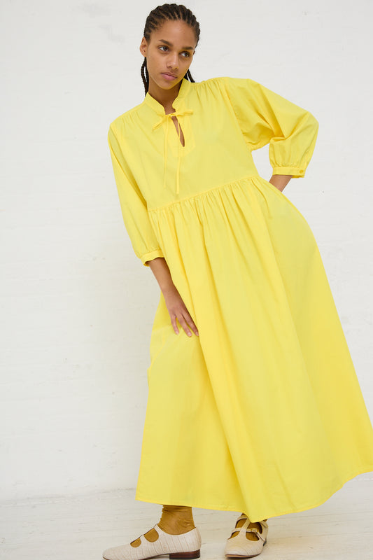 Woman posing in a AVN Sunshine Dress in Yellow, a bright yellow, lightweight cotton maxi dress with long sleeves and a keyhole neckline, against a white background.