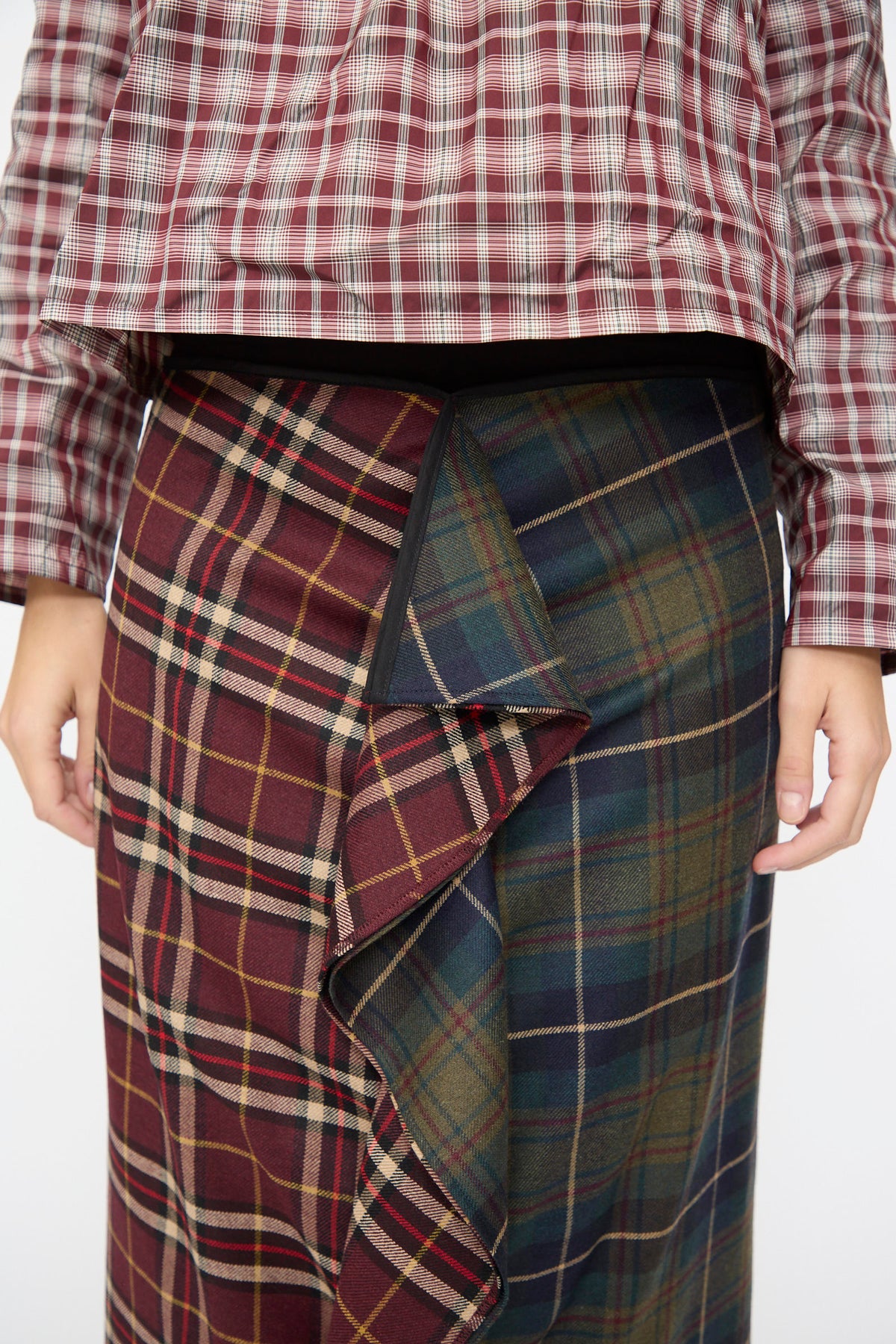 A person wearing the AVN Volant Skirt in Bordeaux and Military Green Check, a plaid wool midi skirt with a vertical ruffle detail.