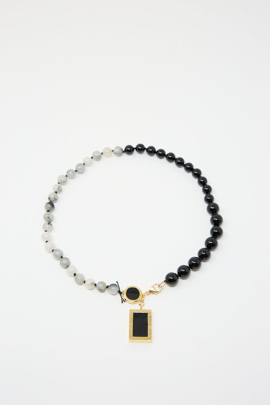 A handmade-in-NYC bead necklace with alternating black and white beads features a gold rectangular pendant with a black center and a small round charm. This elegant 14K Gold Plated Brass, White Eagles Eye and Black Onyx Beaded Necklace with Pendant from Abby Carnevale embodies timeless style and craftsmanship.