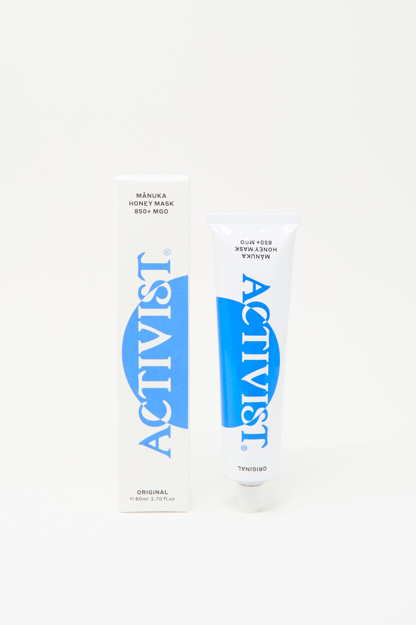 A tube and box of Activist Mānuka Honey Mask, both white with blue text, stand upright against a plain white background, showcasing this natural face mask by Activist.