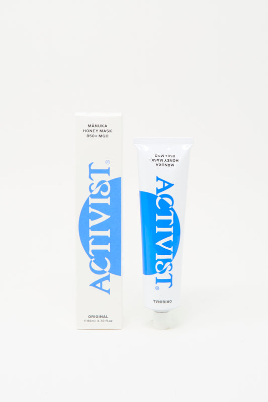 A tube and box of Activist Mānuka Honey Mask, both white with blue text, stand upright against a plain white background, showcasing this natural face mask by Activist.