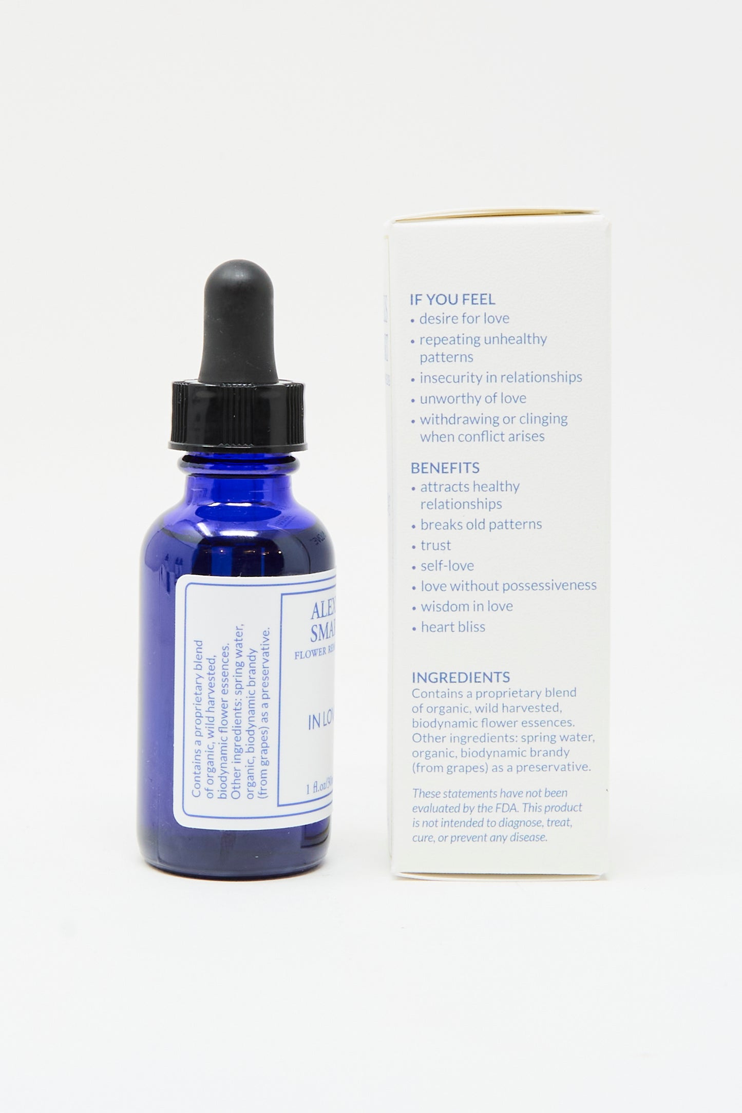 A blue glass dropper bottle labeled "Flower Remedies - In Love" by Alexis Smart stands next to a box displaying the flower essences, benefits, uses, and ingredients in plain text.
