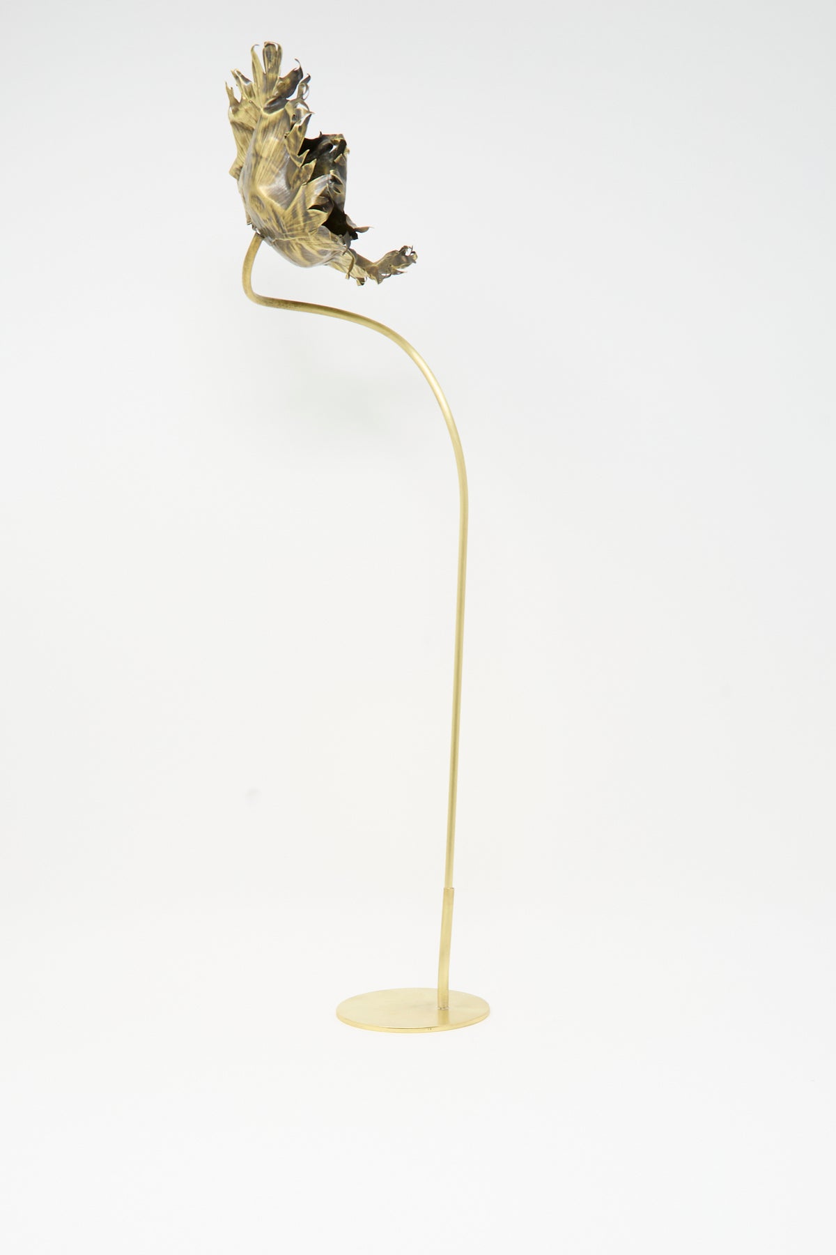 A slender metal stand with a round base topped by a handmade Sterling Silver and Brass Papaver No. 5 sculpture.