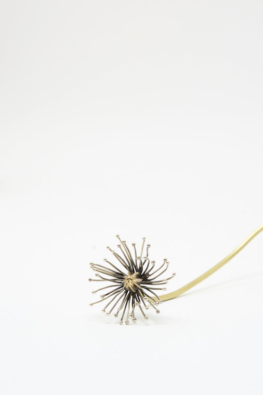 An Alison Layton Sterling Silver and Brass Papaver No. 11 brooch featuring a stylized flower with a dark, textured center, silver-tipped stamens, and a curved brass stem.