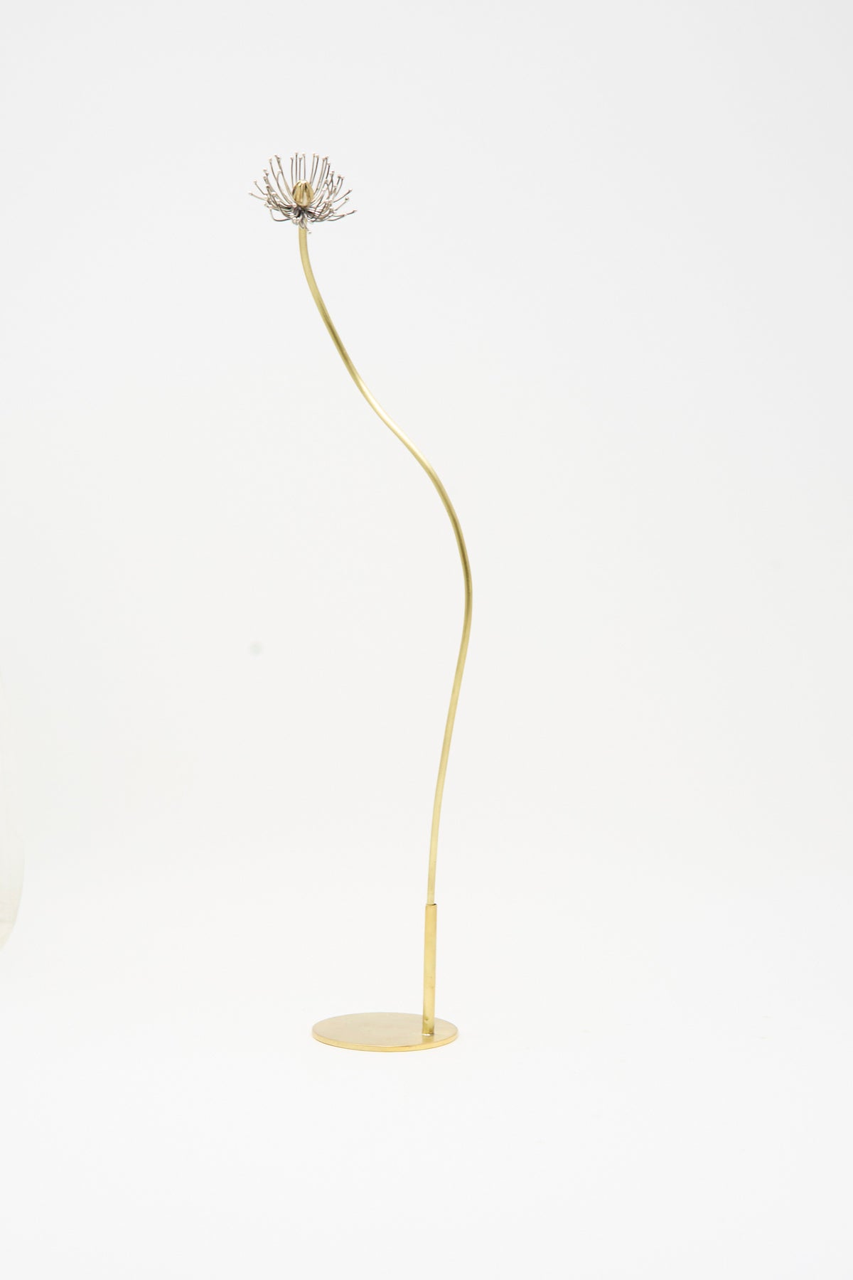 A slender, curved Brass Base - Small by Alison Layton, topped with a small Papaver sculpture on a circular base.
