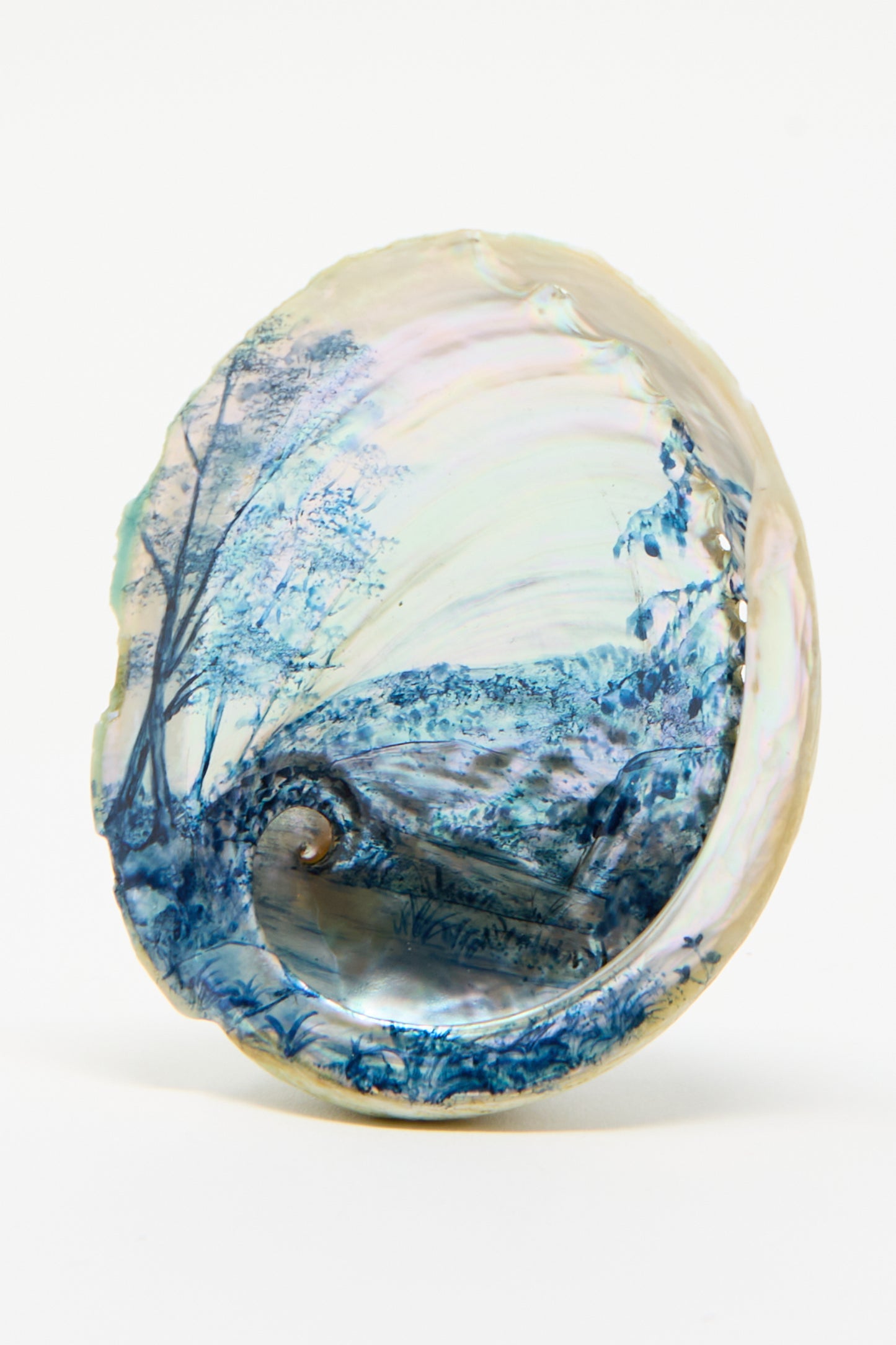 The Hand Painted Abalone I by Alyssa Goodman features a serene blue watercolor landscape of trees, a bridge, and a river beautifully depicted on its inner surface.