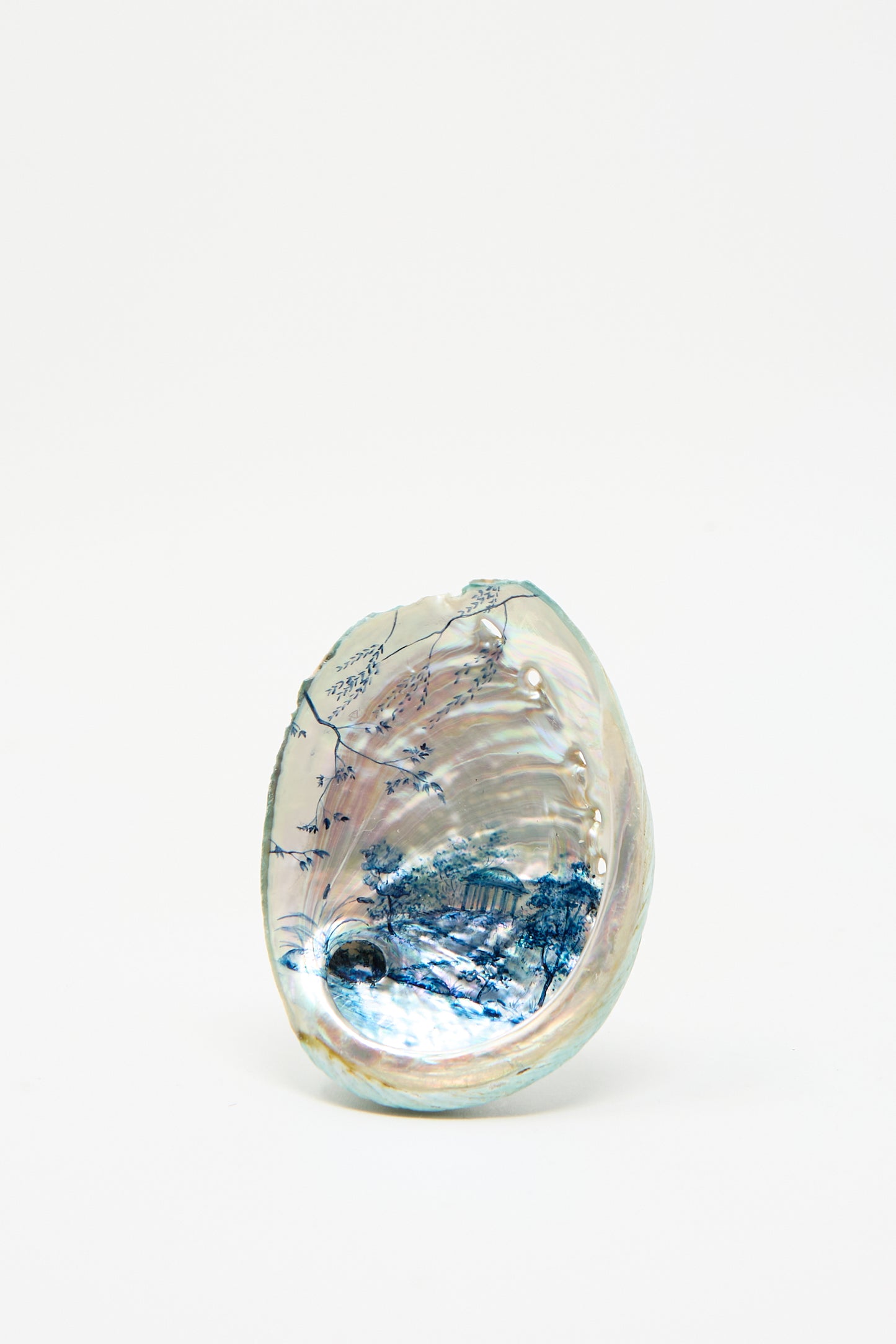 Hand Painted Abalone II by Alyssa Goodman features a decorative shell with intricate blue and silver designs reminiscent of blue watercolor landscapes, set against its plain white interior.