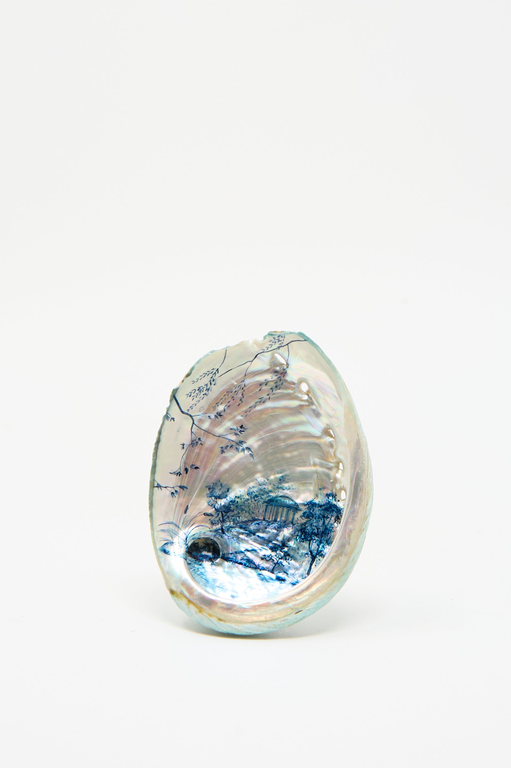 Hand Painted Abalone II by Alyssa Goodman features a decorative shell with intricate blue and silver designs reminiscent of blue watercolor landscapes, set against its plain white interior.