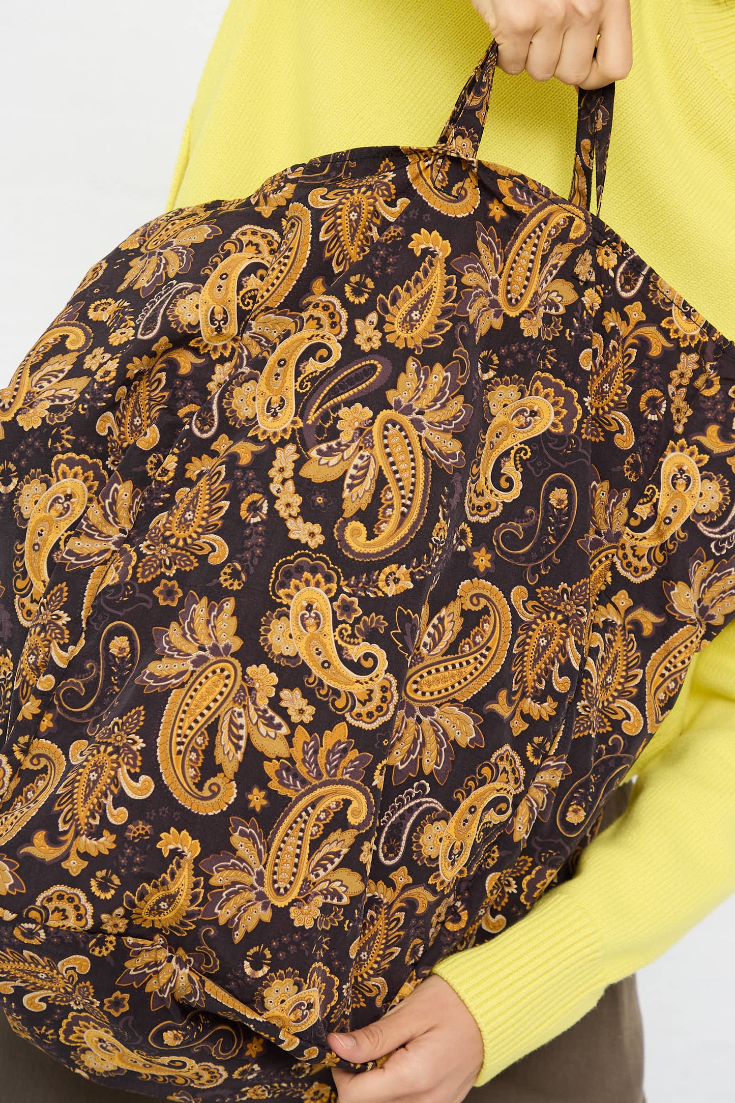 A person holds an Amiacalva Easy Large Bag in Paisley Brown while wearing a yellow shirt.