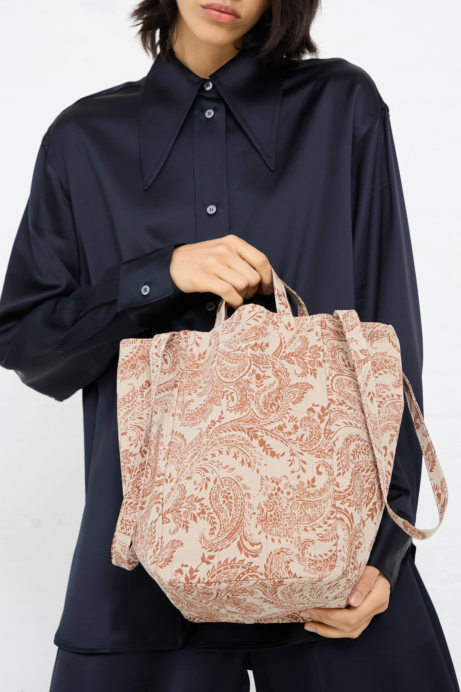 A person wearing a dark silky shirt holds an Amiacalva Easy Medium Bag in Paisley Red.