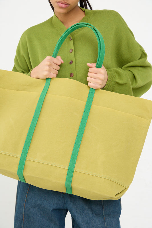 A person holding an oversized yellow Light Ounce Canvas Tote in Lime and Green with green straps, made by Amiacalva in Japan.