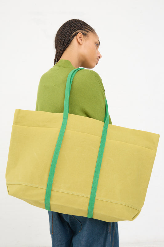 Woman with braided hair carrying a large yellow Amiacalva Light Ounce Canvas Tote in Lime and Green over her shoulder.