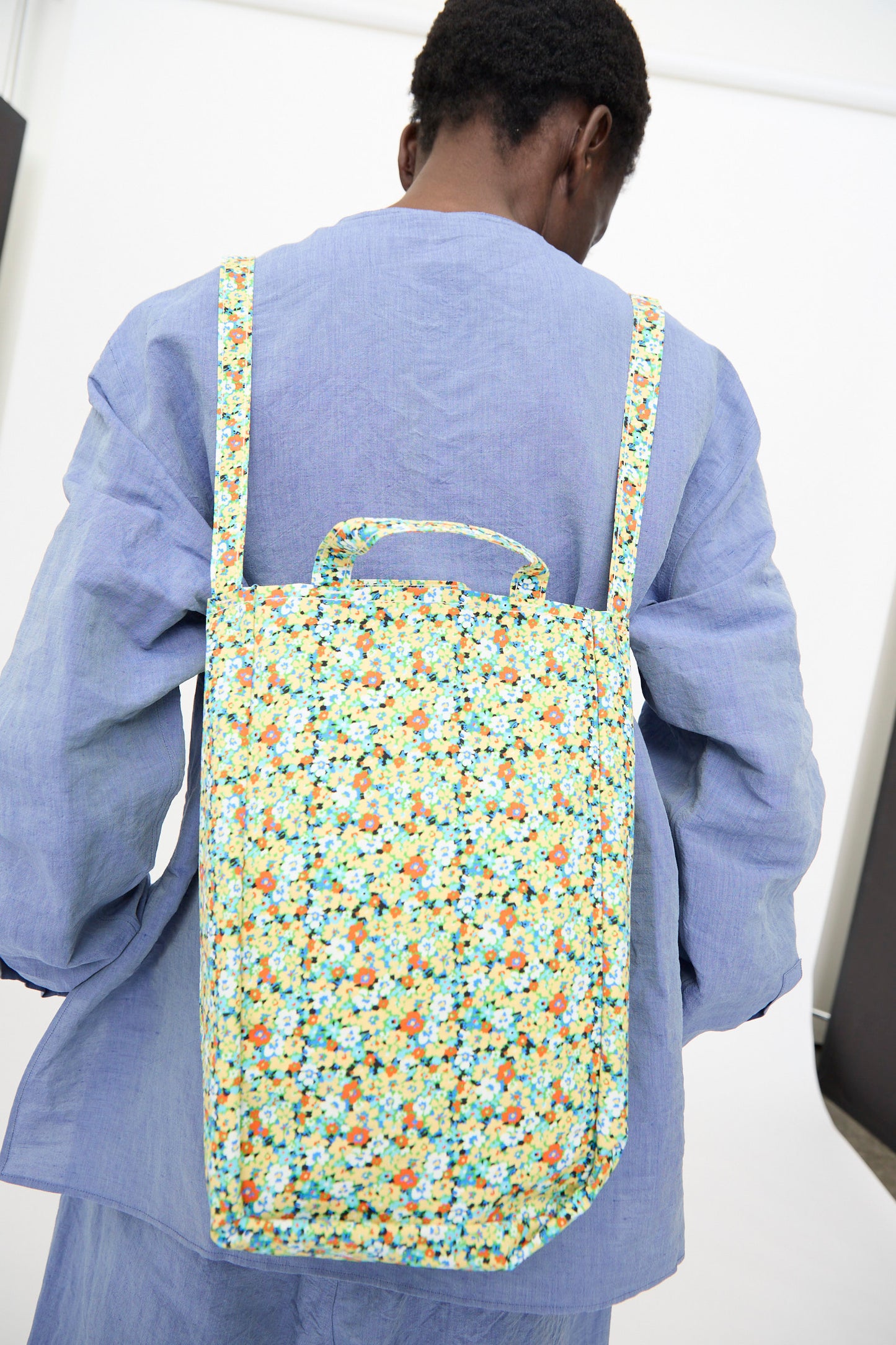 A person wearing a light blue shirt carries the Amiacalva Medium Easy Bag in Flower Green, photographed from behind against a plain background.