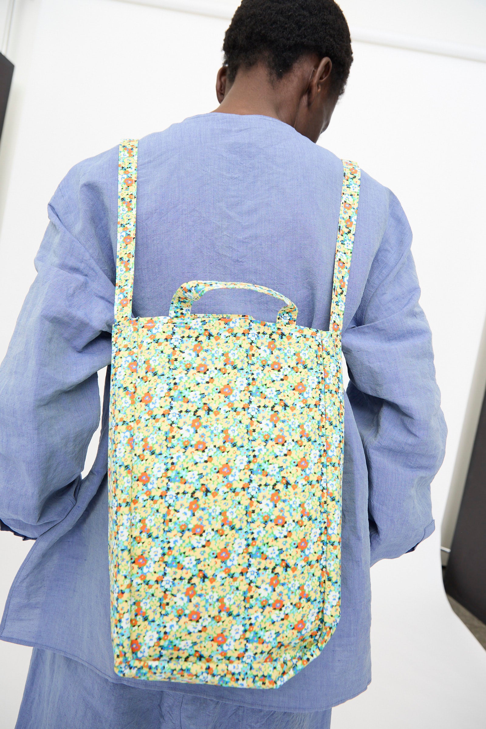 A person wearing a light blue shirt carries the Amiacalva Medium Easy Bag in Flower Green, photographed from behind against a plain background.