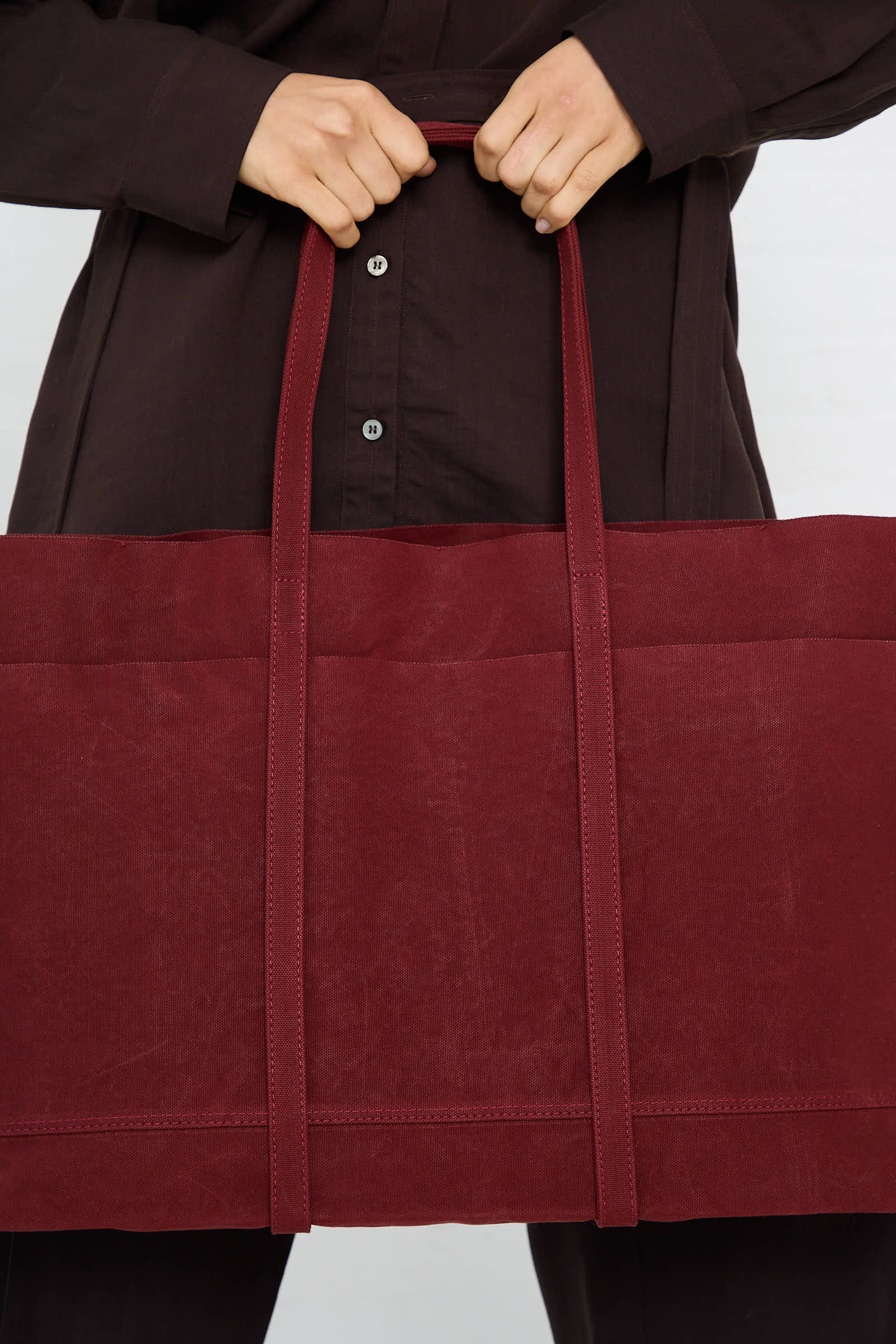 Person holding a Washed Canvas 6 Pocket Large Tote in Burgundy with both hands by Amiacalva.