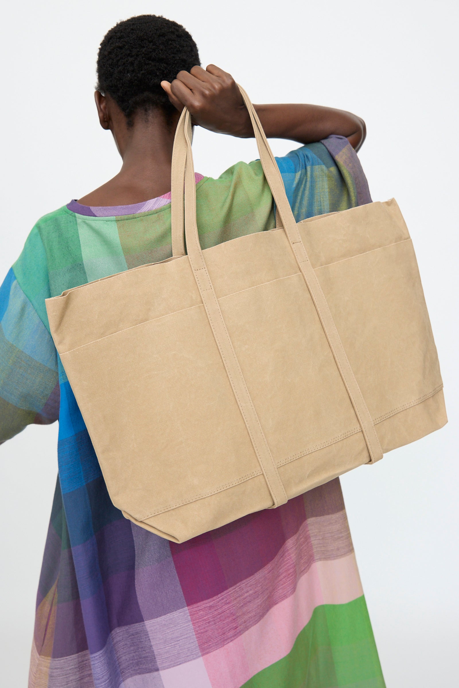 A person facing away from the camera holds the Amiacalva Washed Canvas 6 Pockets Large Tote in Taupe over their shoulder, standing against a plain background.