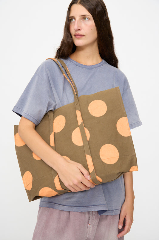 A woman in a blue t-shirt holds the Amiacalva Washed Canvas Medium Dot Tote in Orange, standing against a plain white background.
