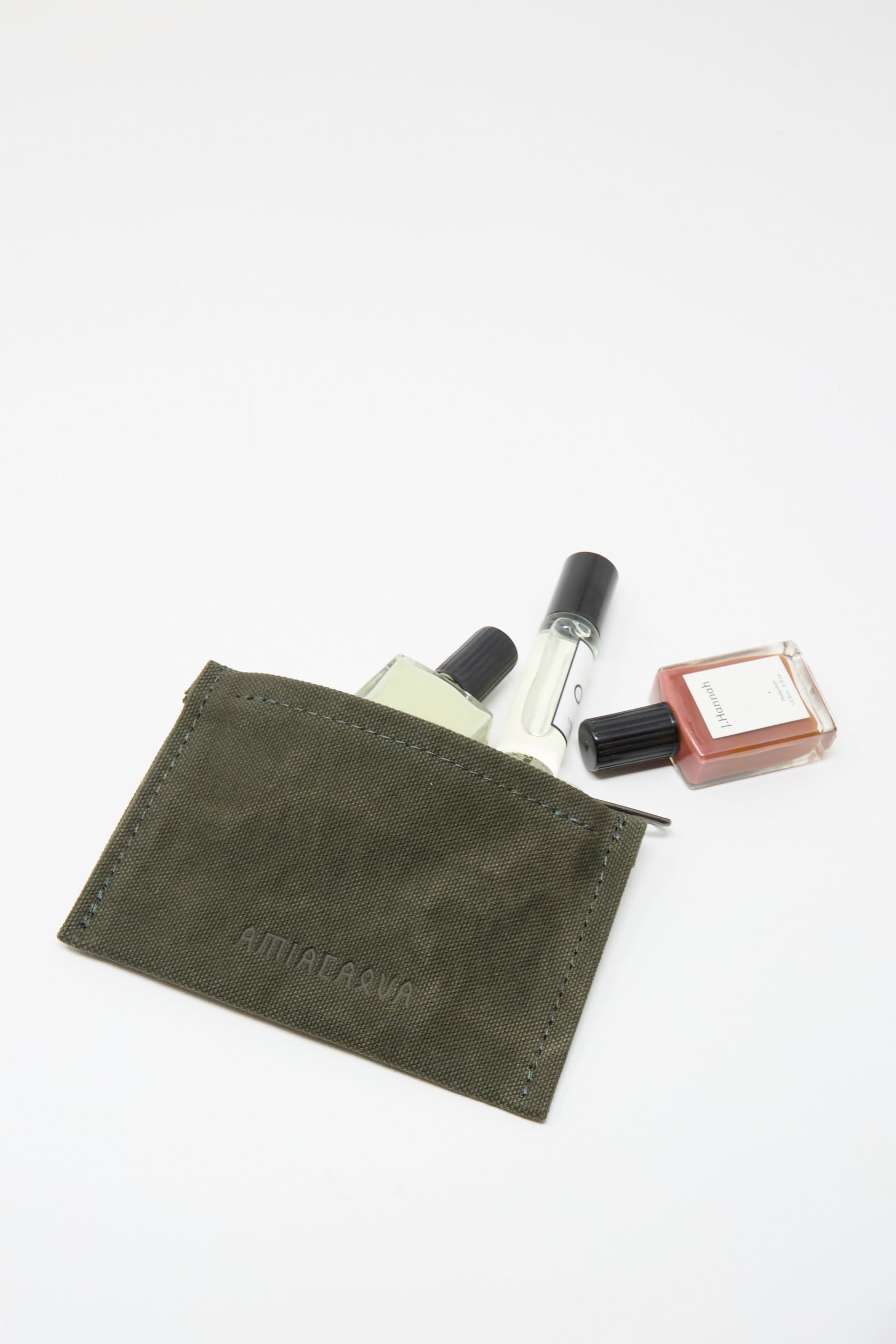 The Amiacalva Washed Canvas Small Pouch in Olive, made in Japan, features a zipper top and holds three small perfume bottles—two clear glass and one amber—partially visible against a white background.