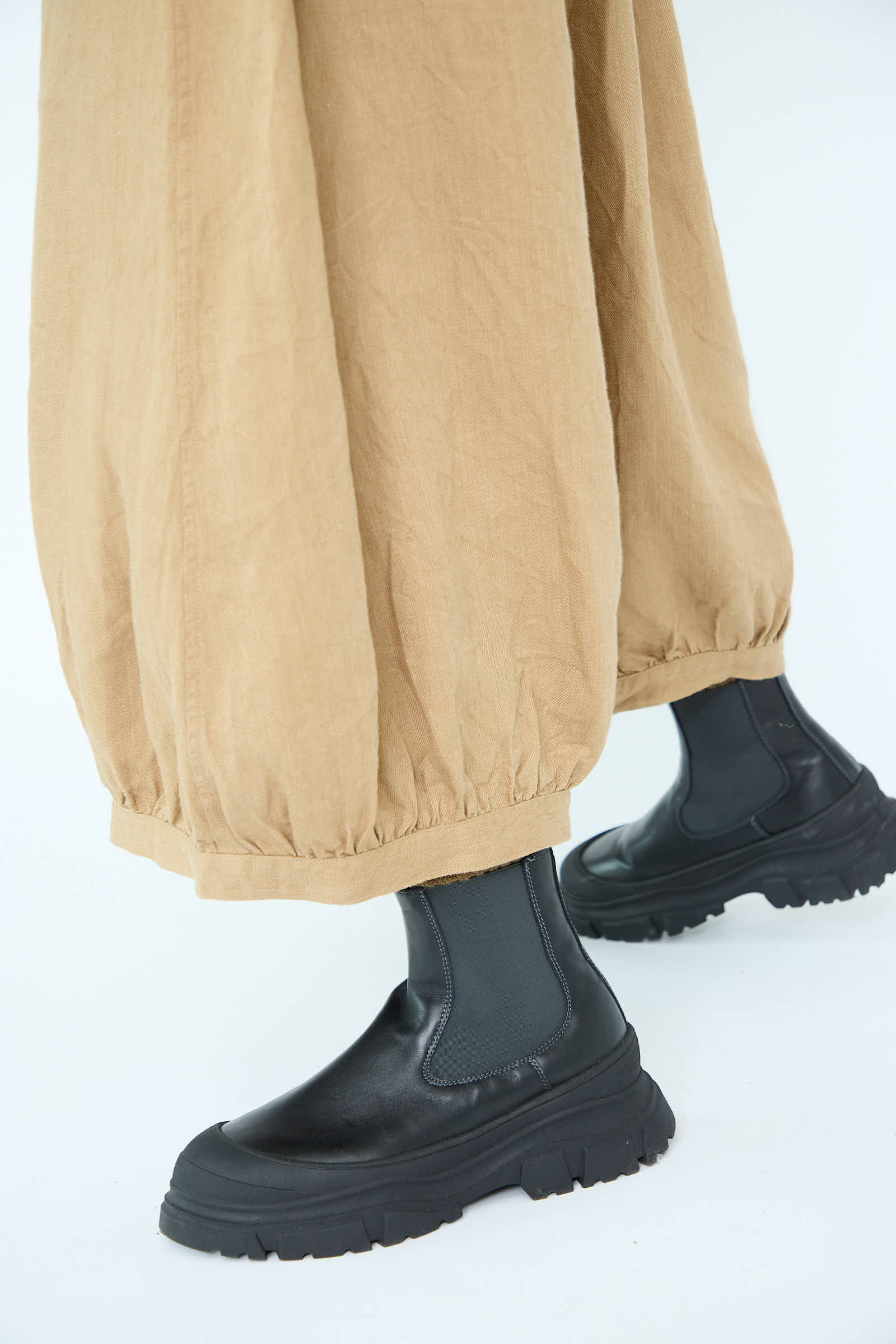 Individual wearing Antiquités Noir Linen Chino Denim Balloon Pants in Beige paired with black platform boots.