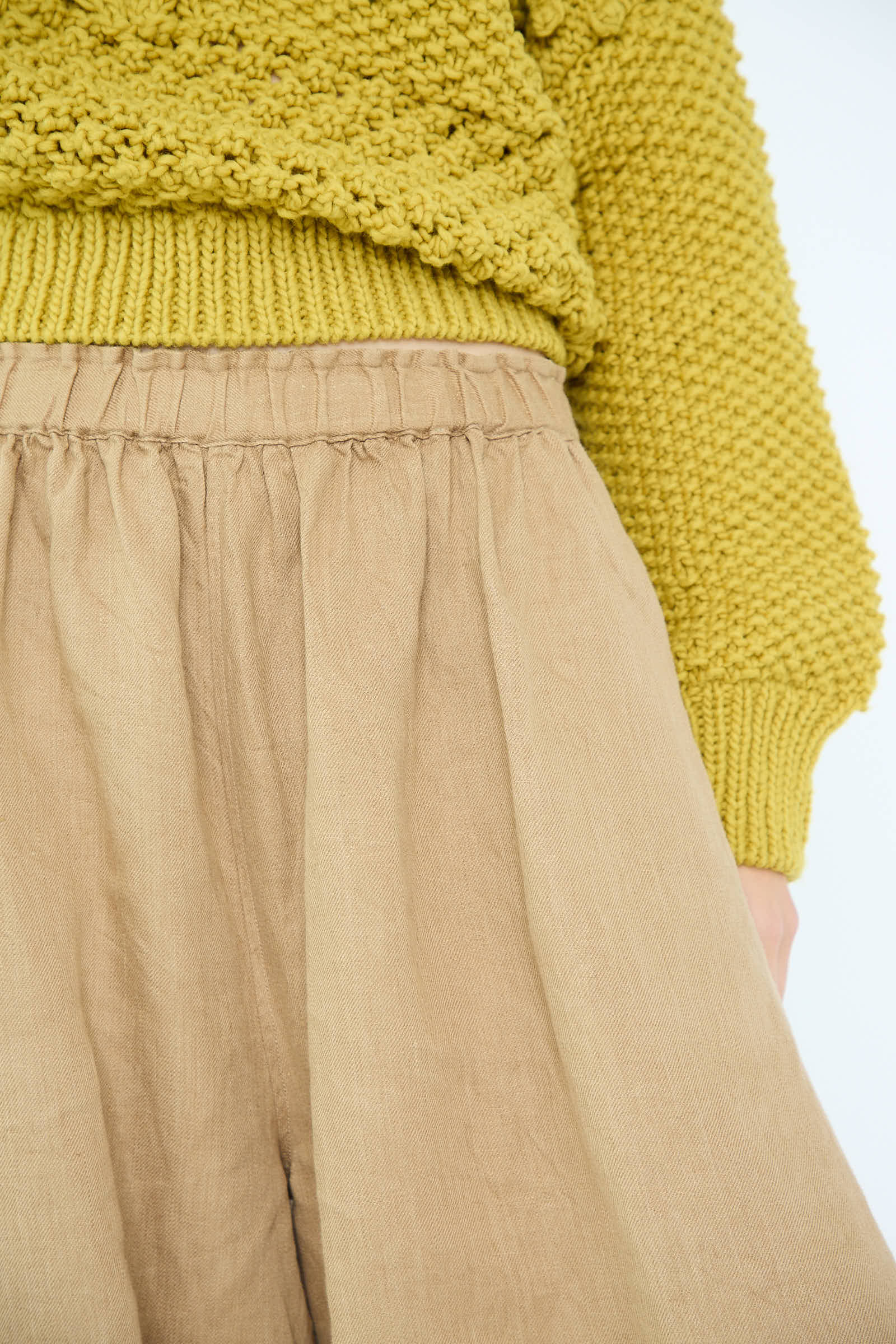 A person wearing a textured yellow sweater and Linen Chino Denim Balloon Pants in beige by Antiquités Noir.