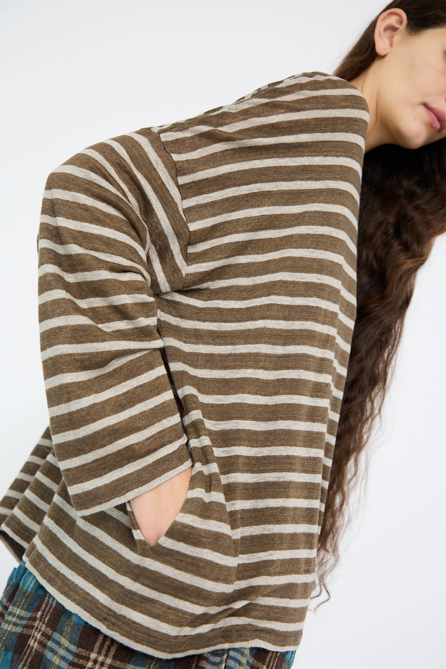 An individual wearing Antiquités Noir's Linen Stripe Pullover in Khaki and Natural, hands tucked in the pockets, leaning slightly forward.