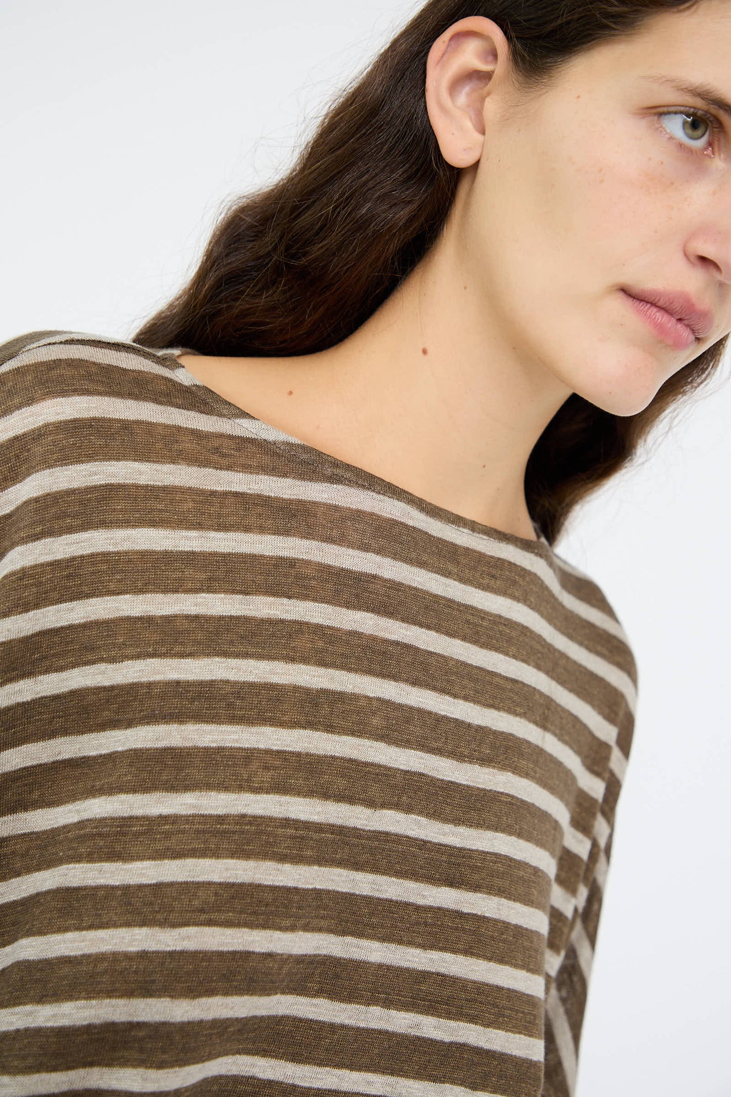 A person with long brown hair wearing the relaxed fit Linen Stripe Pullover in Khaki and Natural by Antiquités Noir, looking sideways against a plain background.