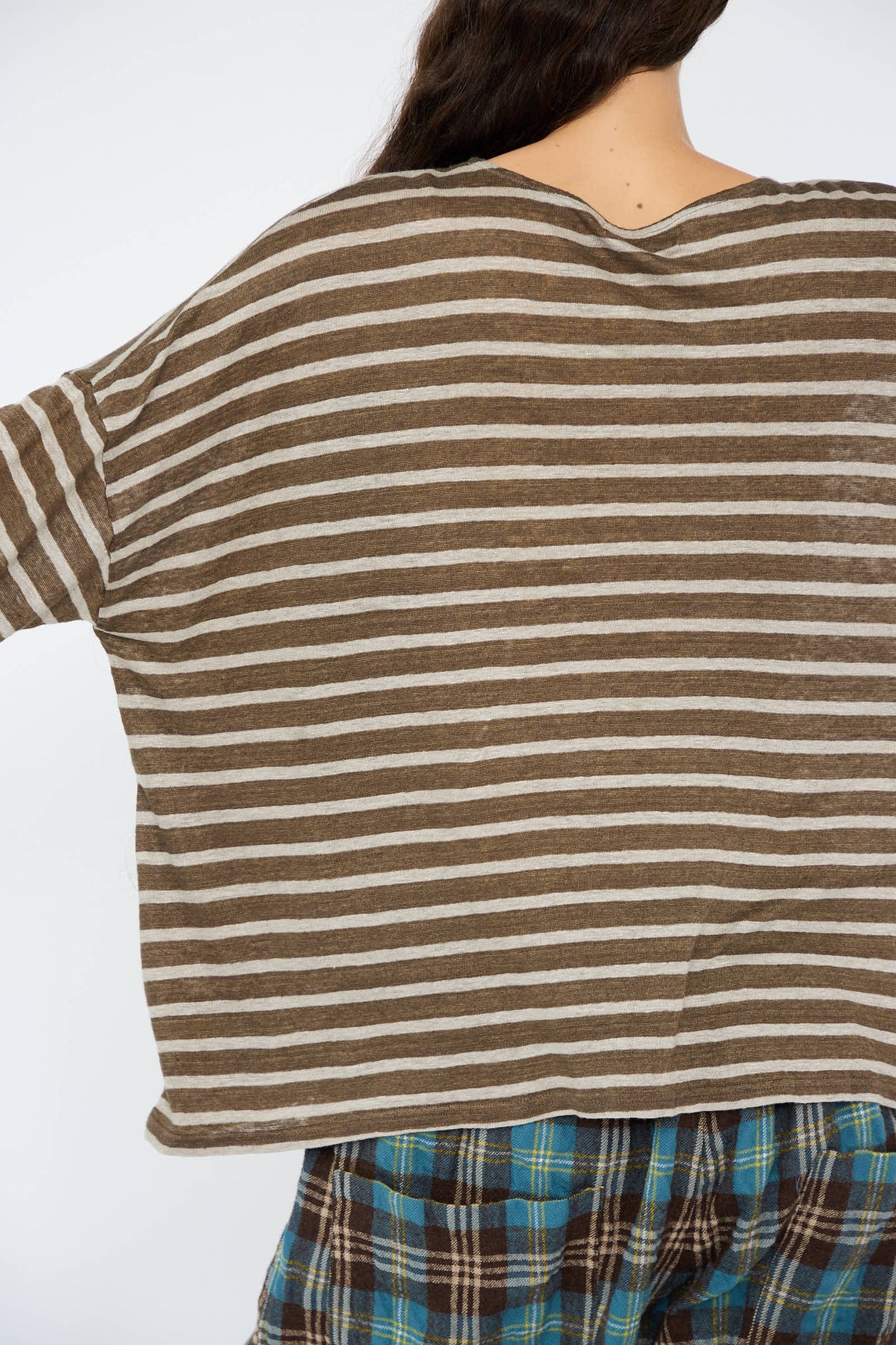 Individual dressed in the Linen Stripe Pullover in Khaki and Natural by Antiquités Noir paired with plaid pants, displaying a back view.