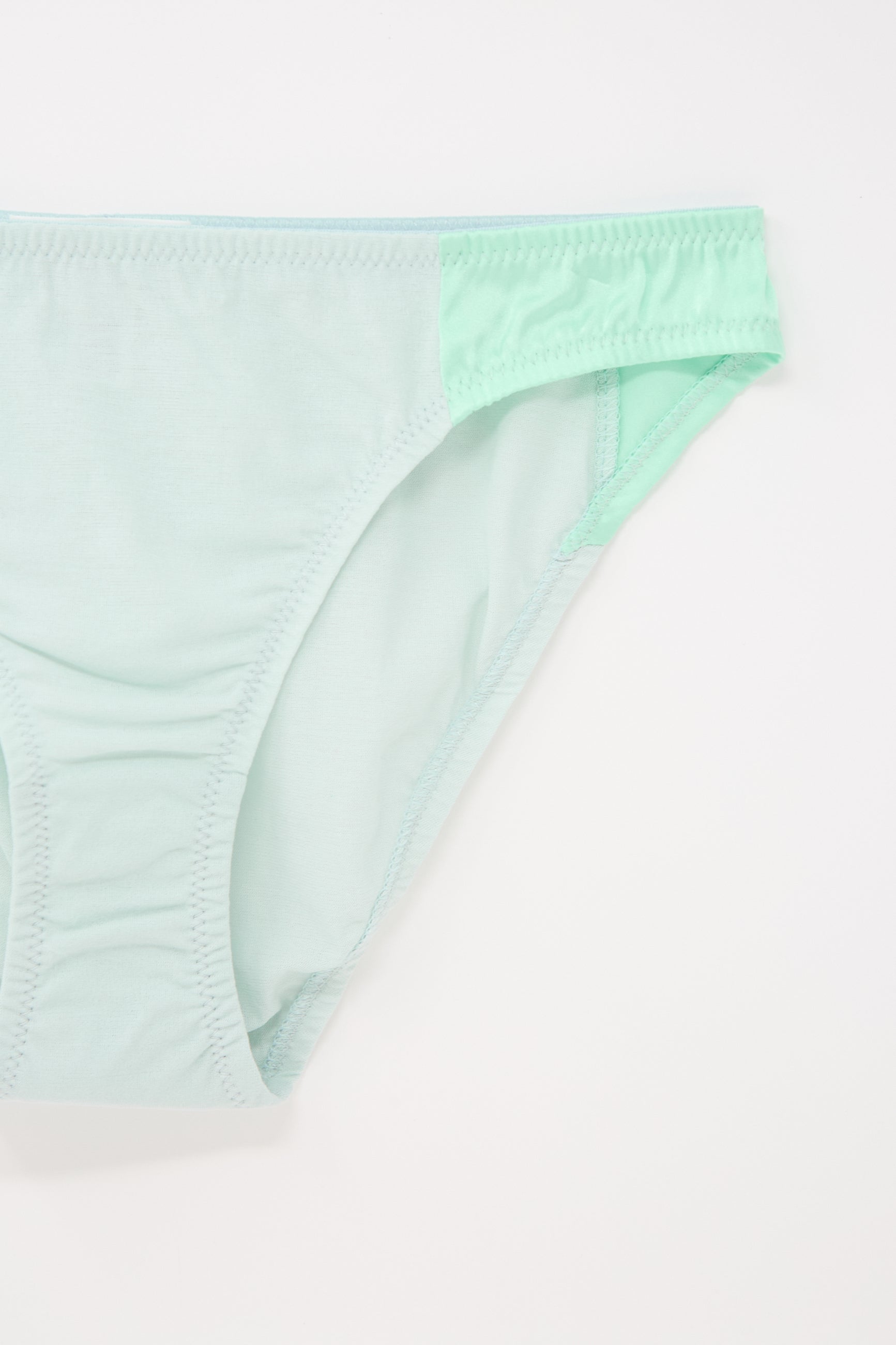 Close-up image of a light green, mid-rise cotton crepe underwear bottom on a white background, showing the front and part of the side. The product is the "Saffi Panty in Cloud" by Araks.