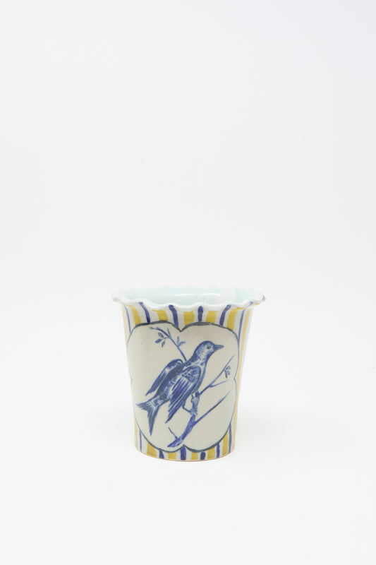The Ariel Clute Hand Painted Bird Vessel is a white ceramic cup with blue and yellow stripes, featuring a hand painted porcelain bird inside a heart-shaped frame on the front.