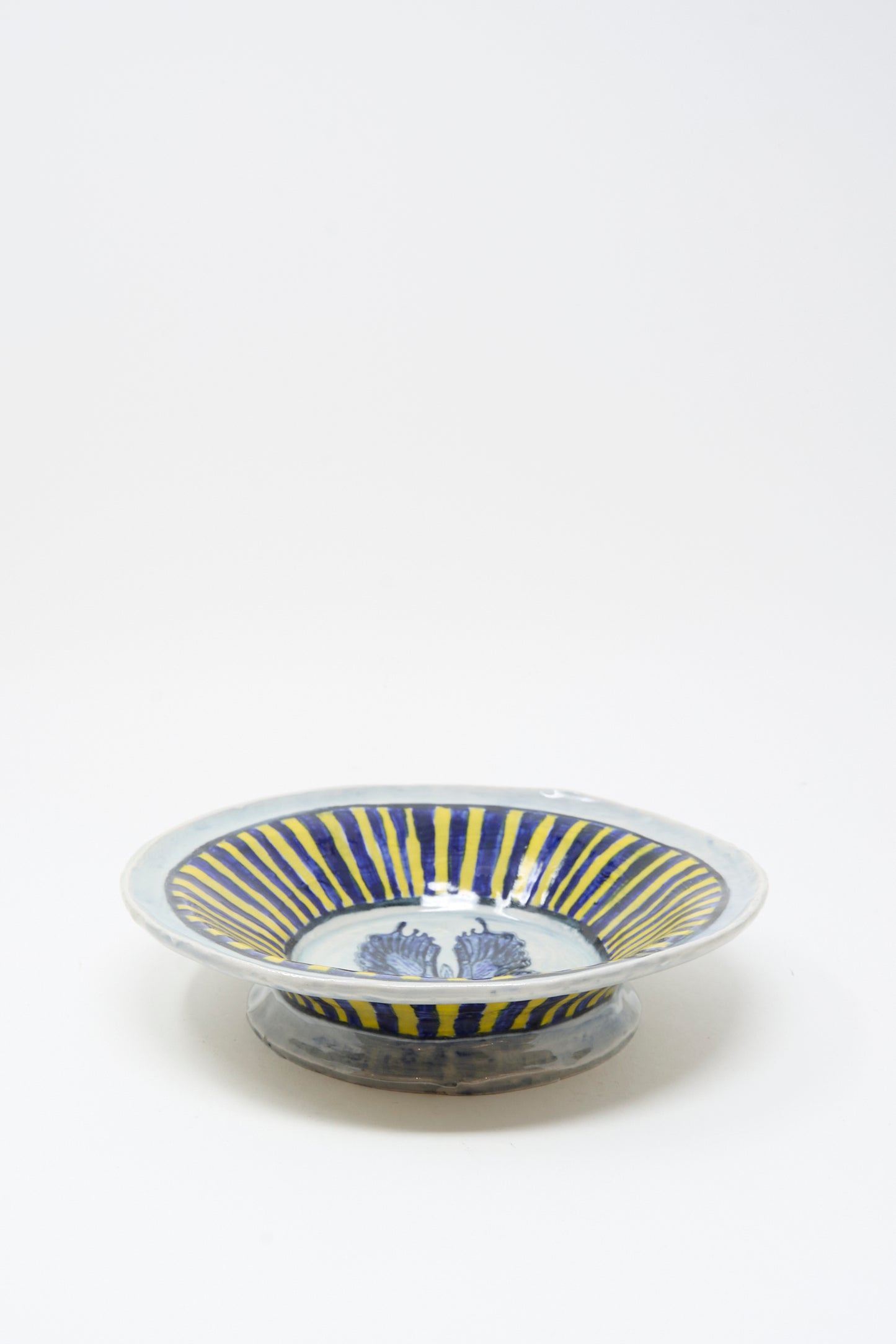 The Ariel Clute Hand Painted Butterfly Bowl features blue and yellow radial stripes and a blue central pattern on porcelain, handmade in California, shown against a plain white background.