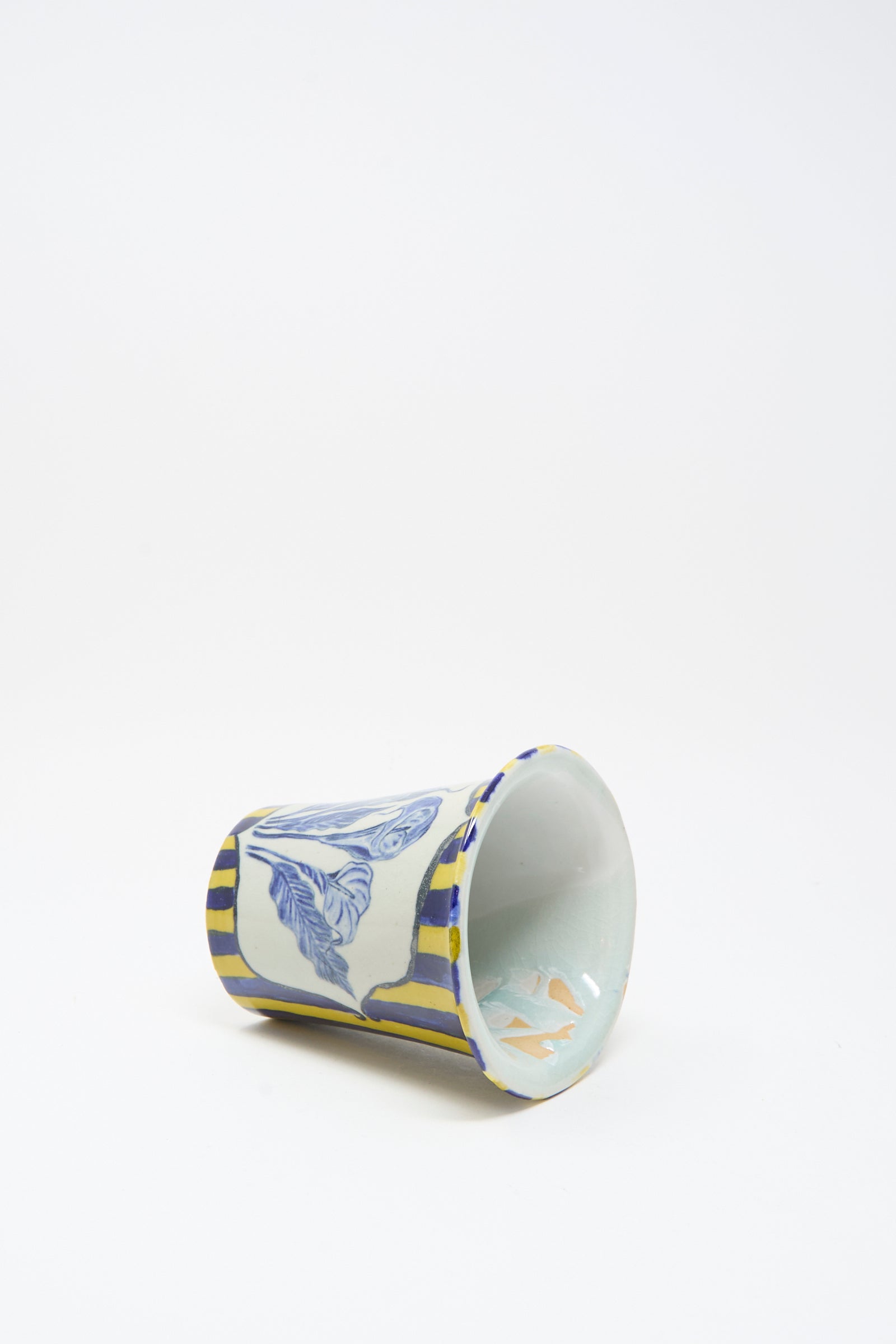 The Ariel Clute Hand Painted Floral Vessel, featuring blue and yellow flowers, is displayed lying on its side against a plain white background.