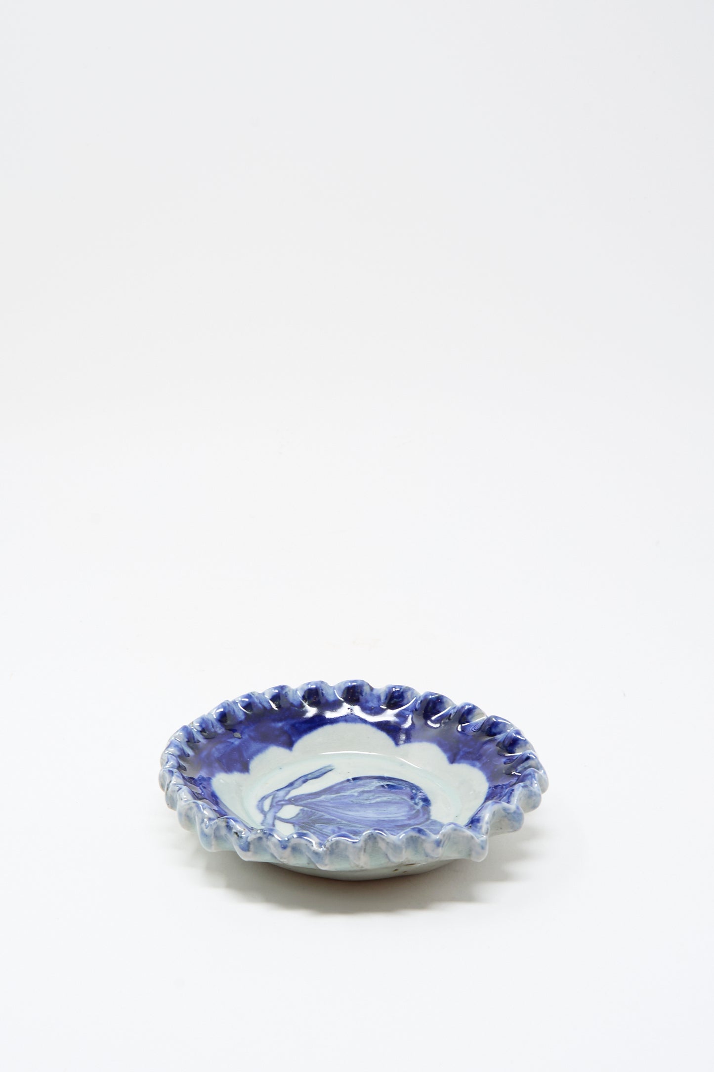The Rustic Fig Plate by Ariel Clute is a small, hand-painted porcelain dish with a wavy rim and blue-and-white marbled glaze, handmade in California and displayed on a plain white background.
