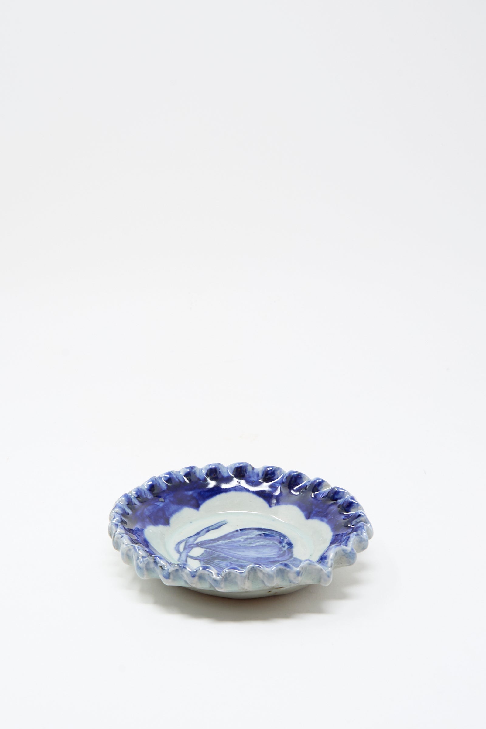 The Rustic Fig Plate by Ariel Clute is a small, hand-painted porcelain dish with a wavy rim and blue-and-white marbled glaze, handmade in California and displayed on a plain white background.