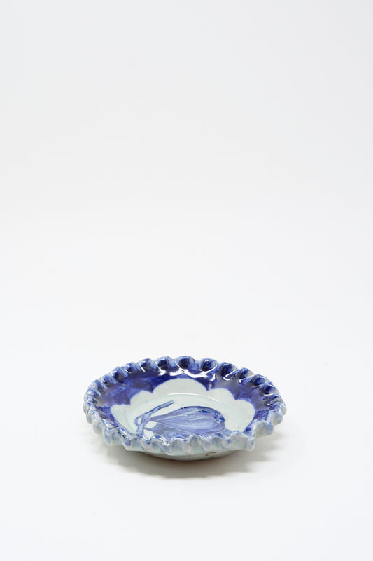 The Rustic Fig Plate by Ariel Clute is a small, hand-painted porcelain dish with a wavy rim and blue-and-white marbled glaze, handmade in California and displayed on a plain white background.