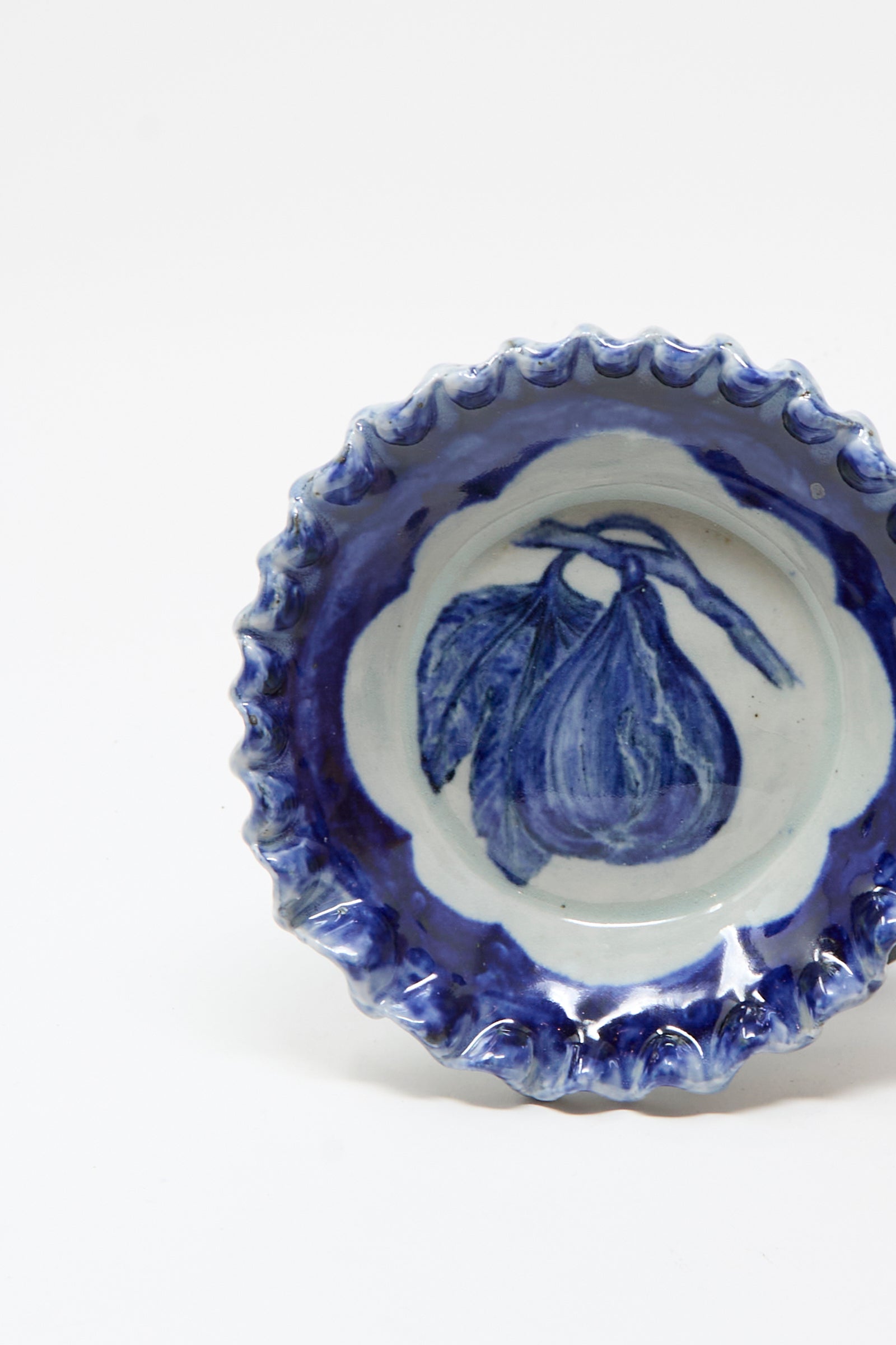 The Rustic Fig Plate by Ariel Clute is a blue and white hand-painted porcelain plate with a scalloped edge, featuring a central fig and leaves design—perfect for adding artisanal charm to your table.