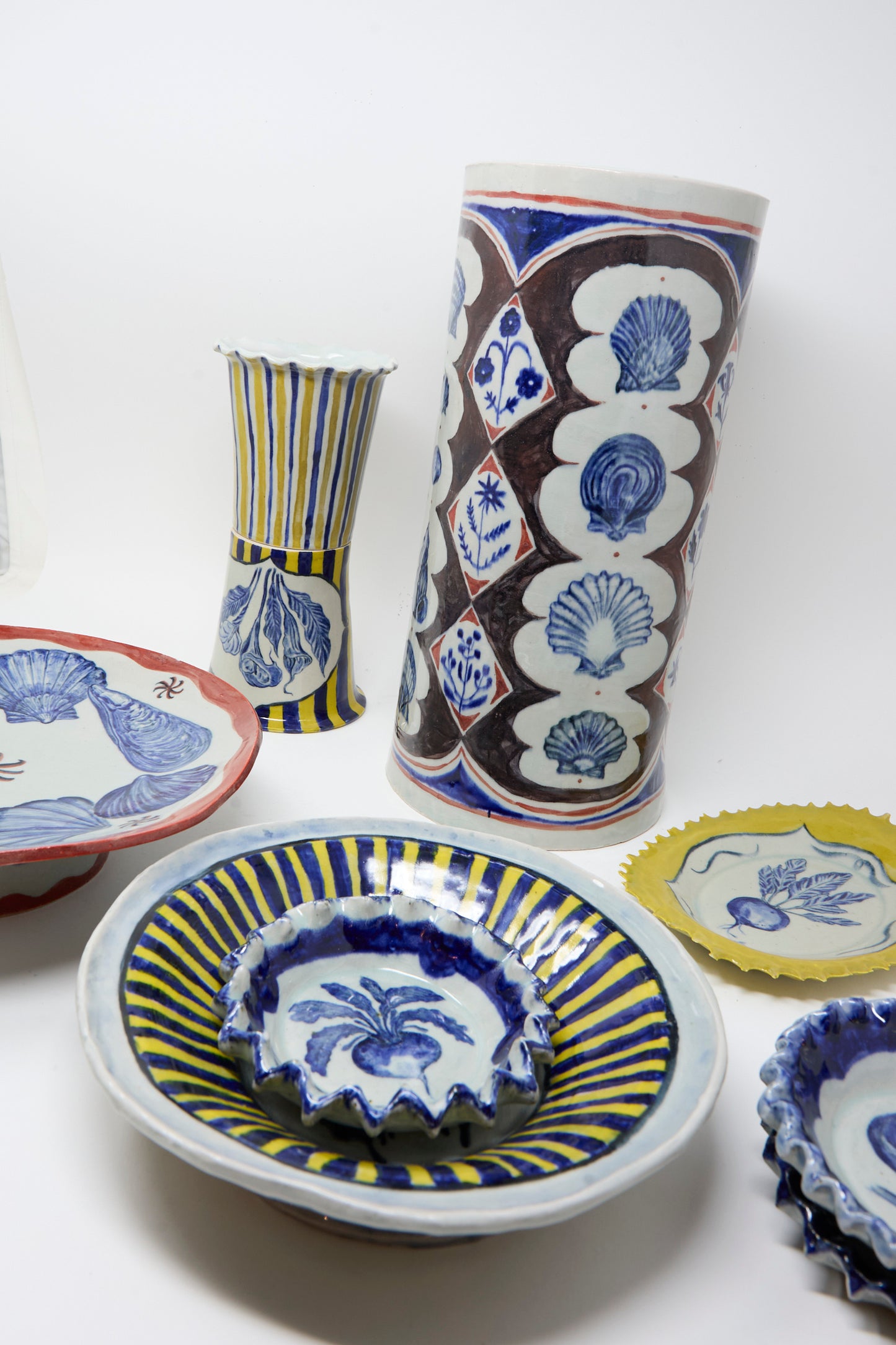 The Ariel Clute Rustic Turnip Bowl features hand-painted blue and yellow floral, shell, and turnip motifs on ceramic, displayed against a white background.