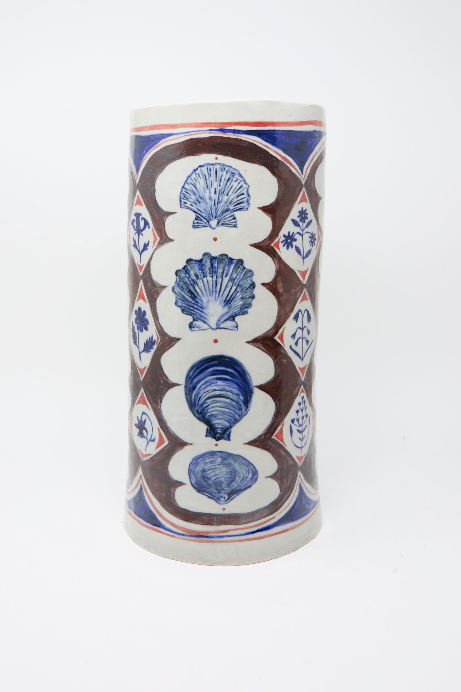 The Sea Shore Vessel by Ariel Clute is a tall, hand-painted porcelain piece with shell motifs and geometric floral patterns in brown, blue, and red on a white background.