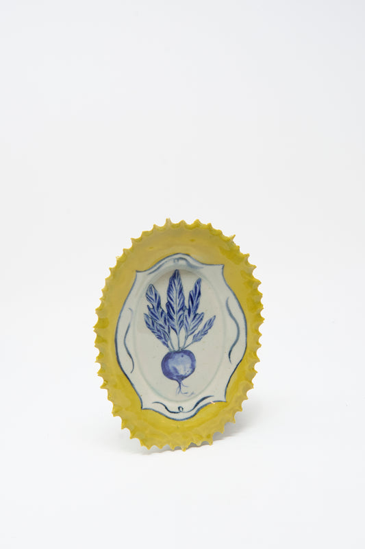 The Yellow Radish Plate by Ariel Clute is a handmade, hand-painted oval porcelain plate featuring a blue radish design in the center and a yellow scalloped edge, crafted in California.