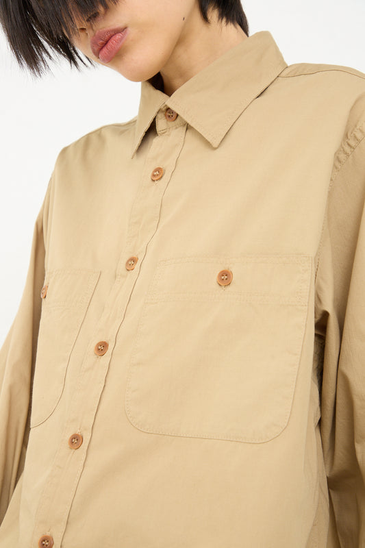 A close-up image of a person wearing an As Ever 101 Shirt in 40's Khaki vintage button-down shirt with front pockets and brown buttons. Only the lower half of the person's face is visible.