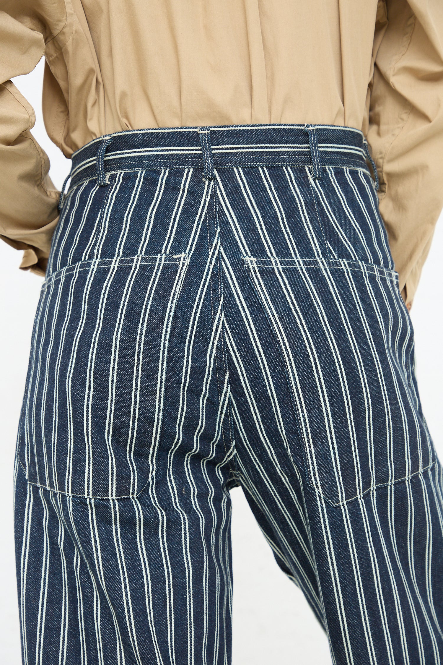 A close-up view of a person from behind, wearing As Ever's Brancusi Pant in Indigo Denim Stripe and a beige shirt.