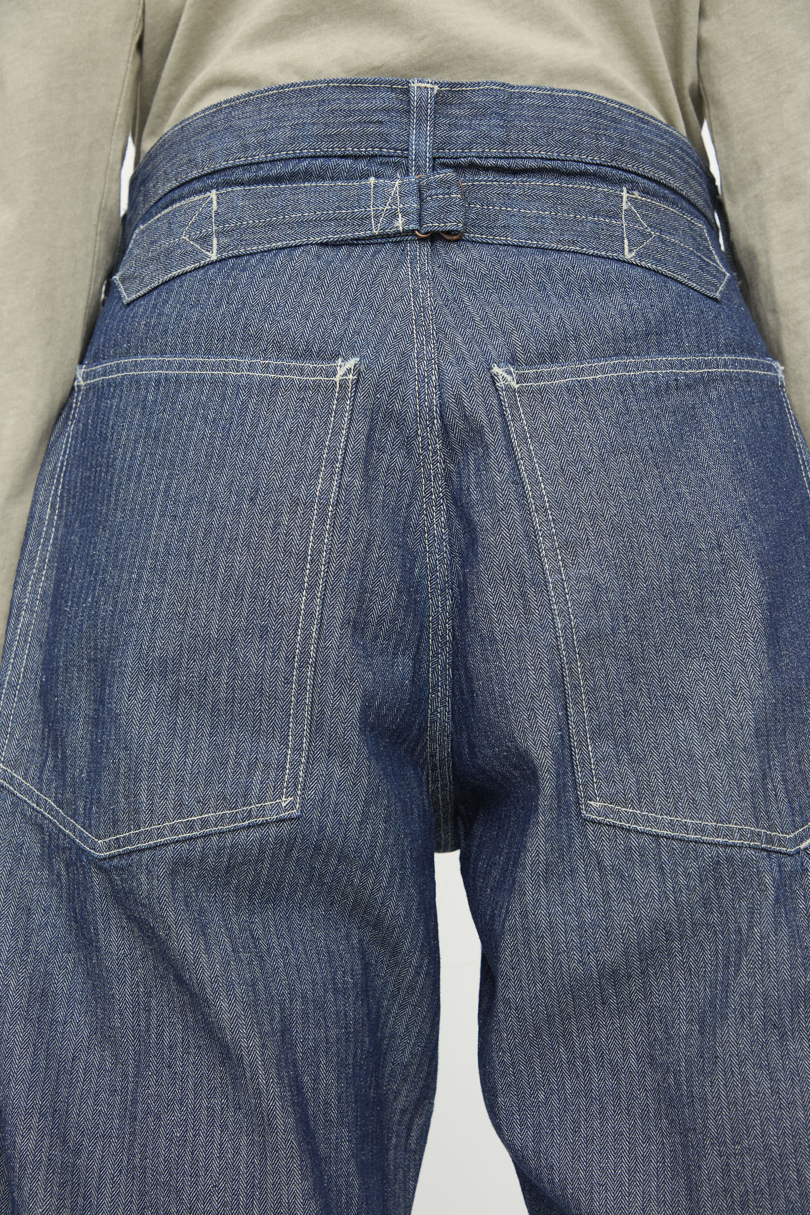 Close-up of the back of a person wearing As Ever's Henri Pant in HBT Denim, featuring large back pockets and white stitching, paired with a beige top.