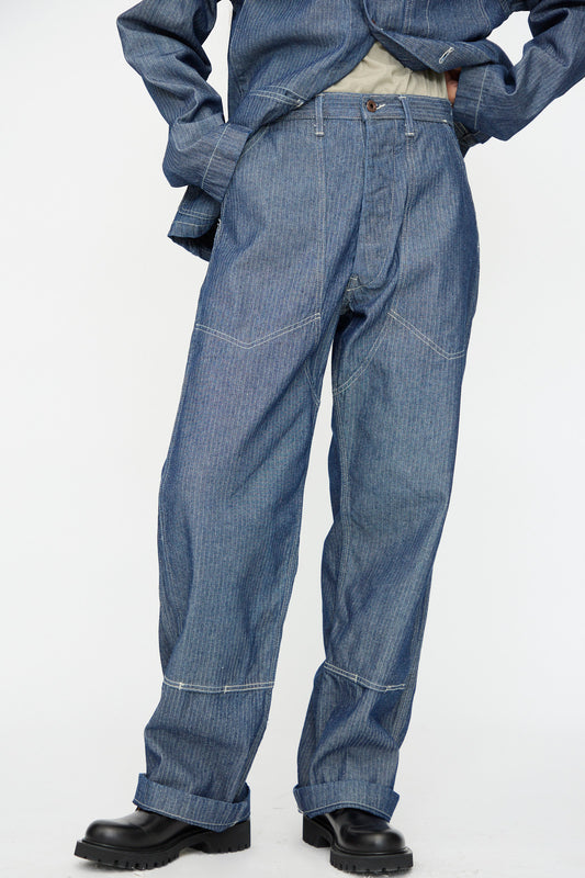 Model wearing the Henri Pant in HBT Denim by As Ever and a matching denim jacket with black chunky shoes, standing against a plain white background.