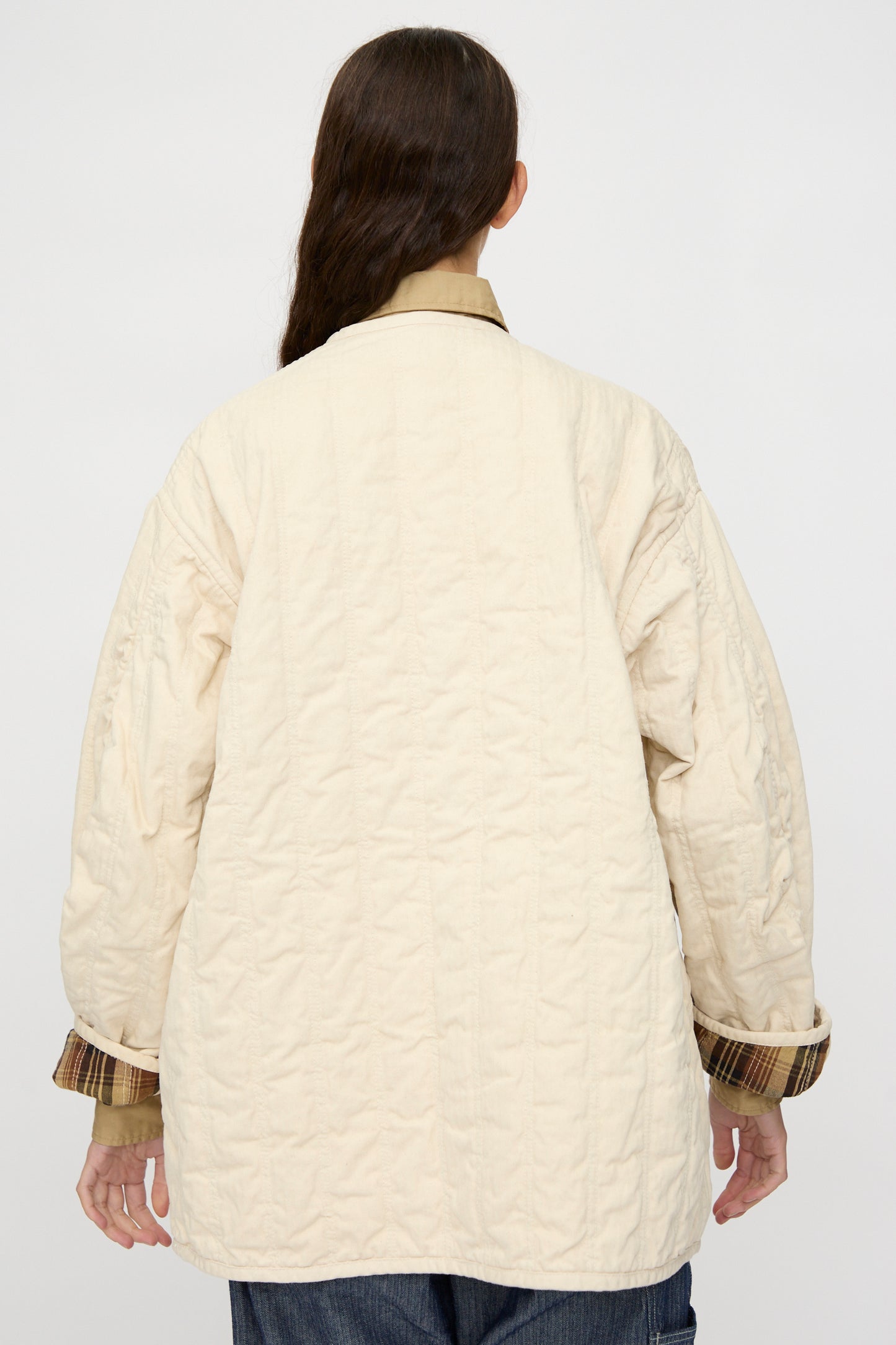 Person with long brown hair, seen from behind in a relaxed-fit As Ever Quilt Coat in HBT Natural with cotton batting, layered over a plaid shirt and set against a plain background.