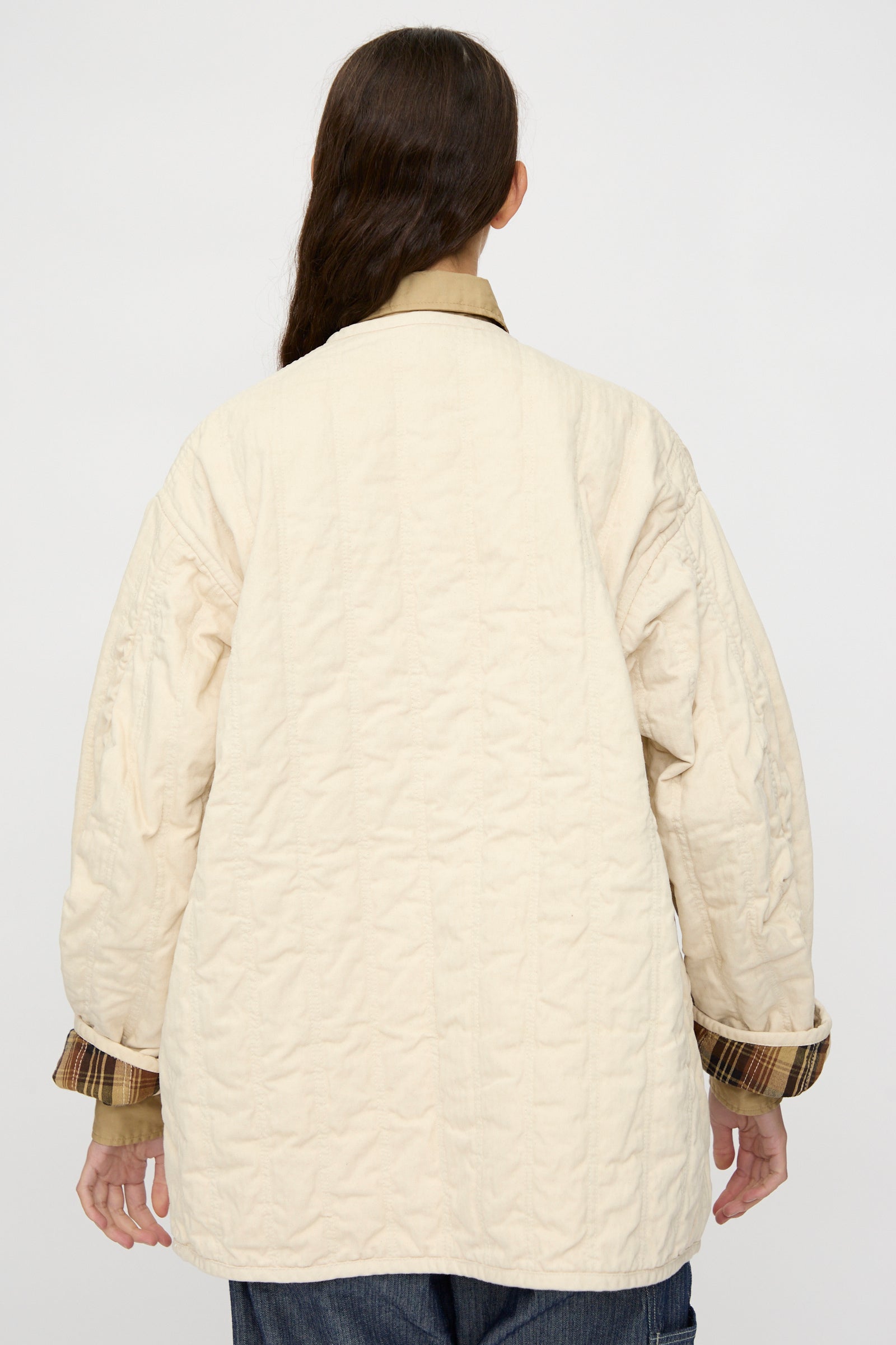 Person with long brown hair, seen from behind in a relaxed-fit As Ever Quilt Coat in HBT Natural with cotton batting, layered over a plaid shirt and set against a plain background.