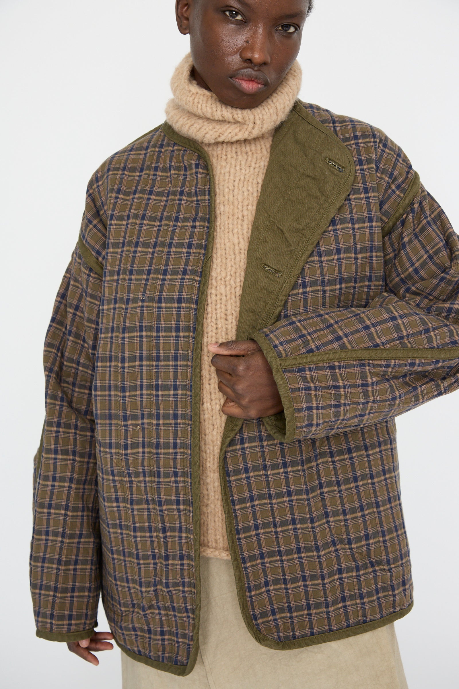 A person wearing As Ever's Quilt Jacket in Olive over a beige turtleneck sweater, standing against a plain background.