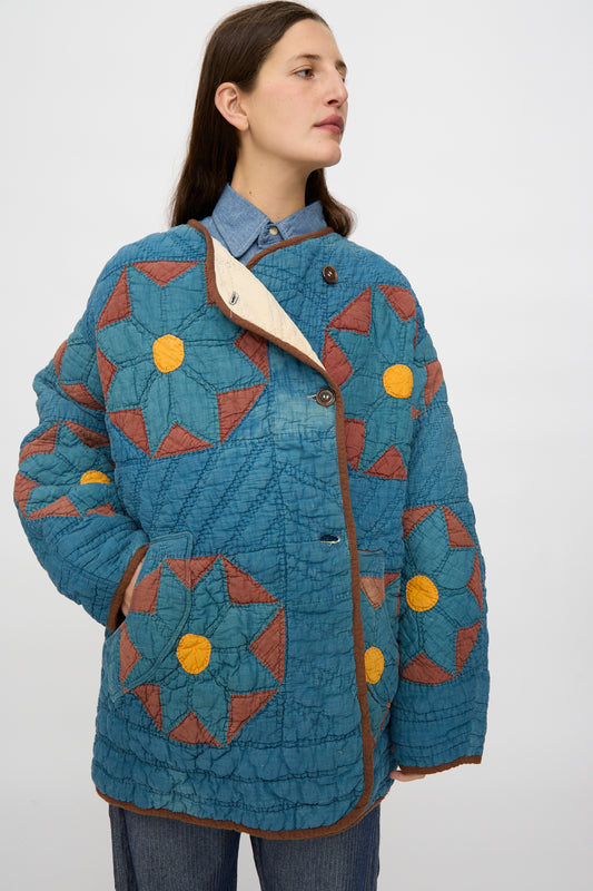 A person wearing the As Ever Vintage Quilt Coat in indigo, brown, and yellow over a denim shirt and blue pants stands against a plain light background.