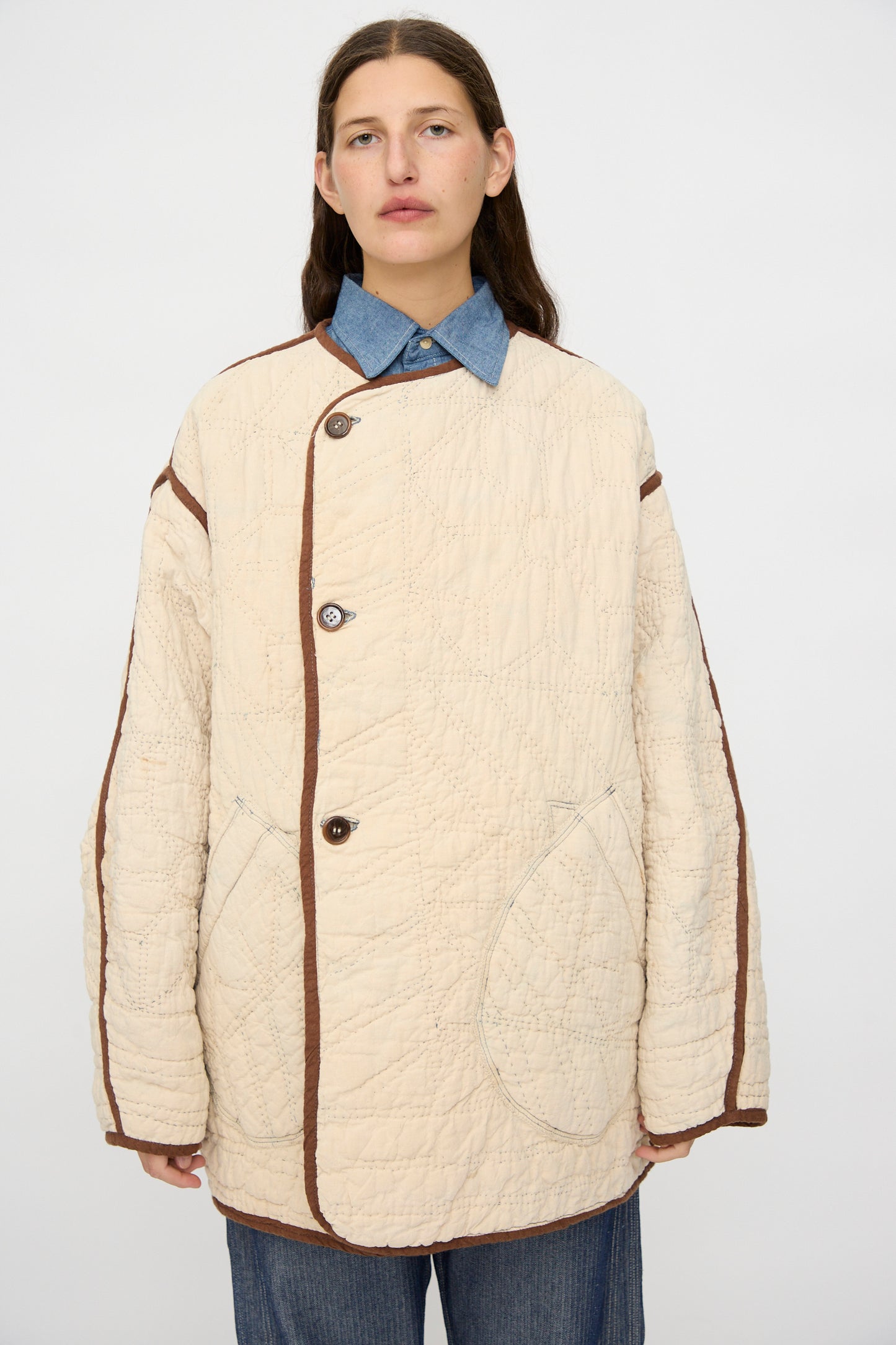 A person wears the As Ever Vintage Quilt Coat in Indigo, Brown and Yellow over a blue collared shirt, standing against a plain light background.